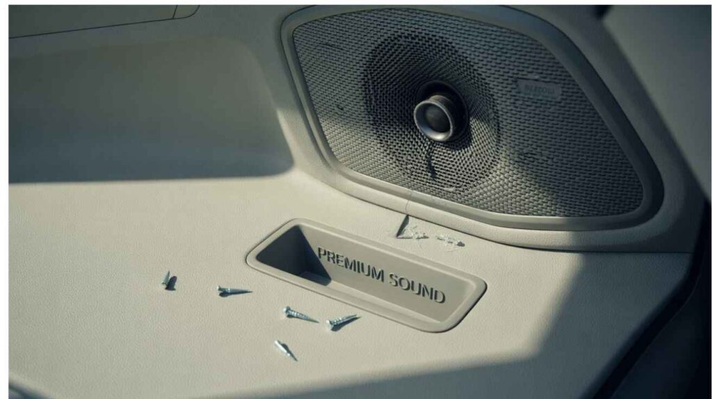 Car door interior with visible speaker grille showing loose screws and subtle vibration, illustrating car speaker rattling issue.