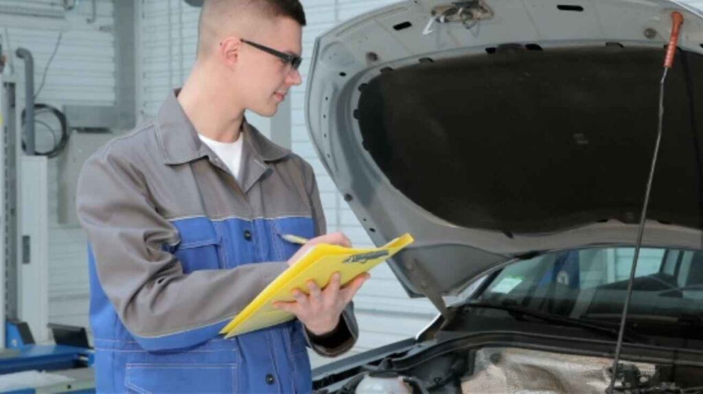 Mechanic writing estimated car horn repair costs on a clipboard with fuse, relay, horn unit, and wiring placed on a workbench.