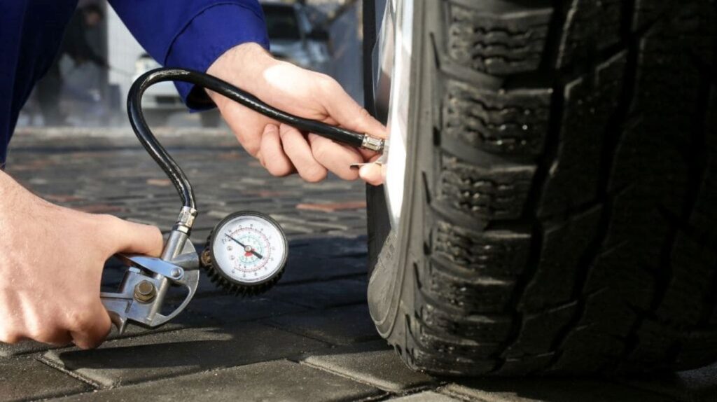 Mechanic checking car tire pressure using a digital tire pressure gauge.