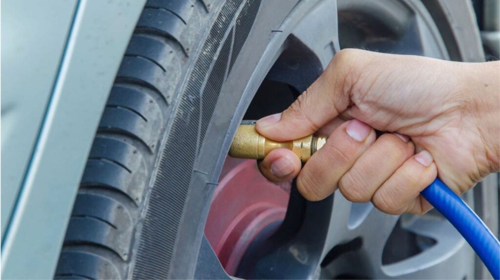 Mechanic inflating car tire with an air pump at a service station.