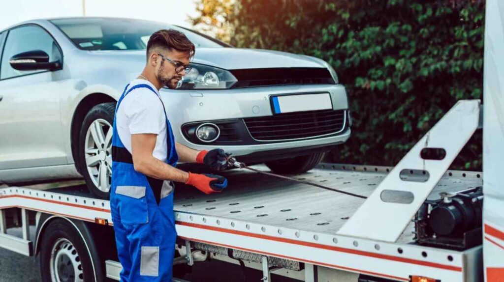 Mechanic checking an AWD towing procedure beside flatbed truck.
