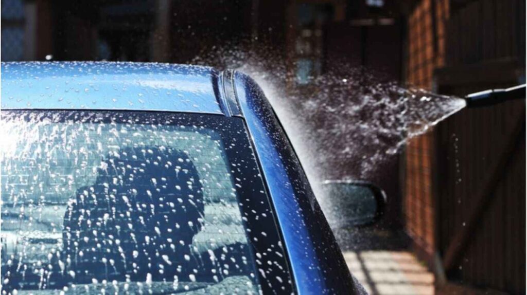 Water jets spraying a car with a cracked windshield during an automatic car wash, showing potential damage risk.