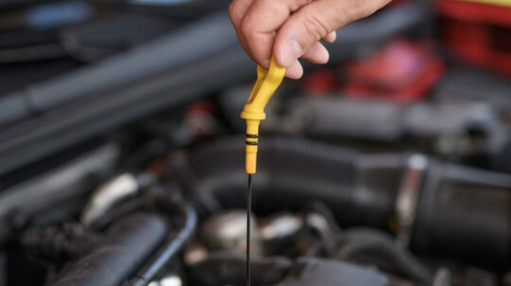 A driver checks engine oil with a dipstick under the car hood on level ground.
