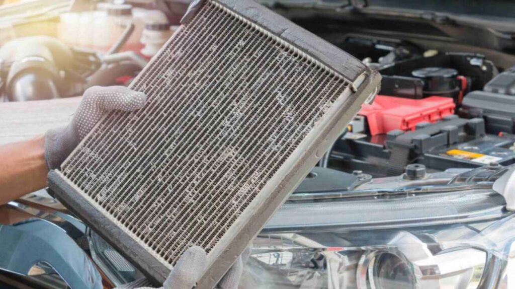 Mechanic repairing clogged heater core behind car dashboard during heating system inspection.