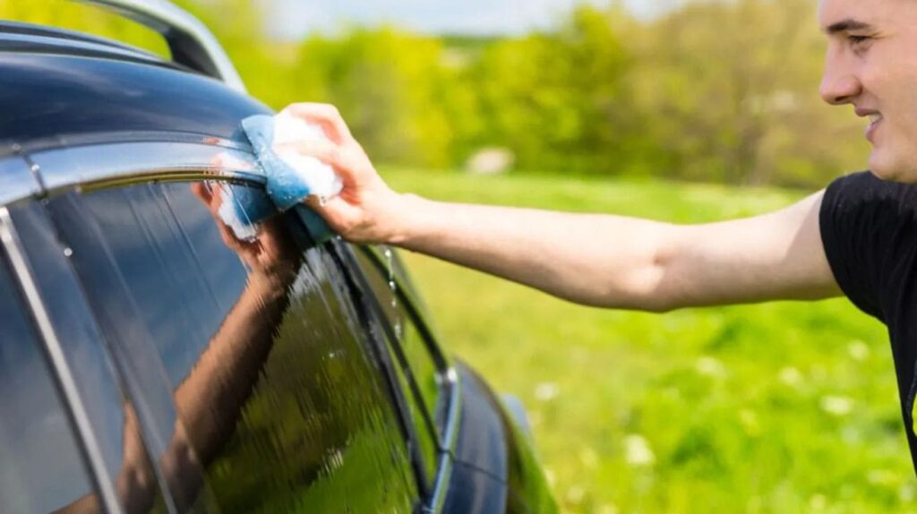 A car owner gently hand-washing the exterior of a newly tinted car using soft mitts.