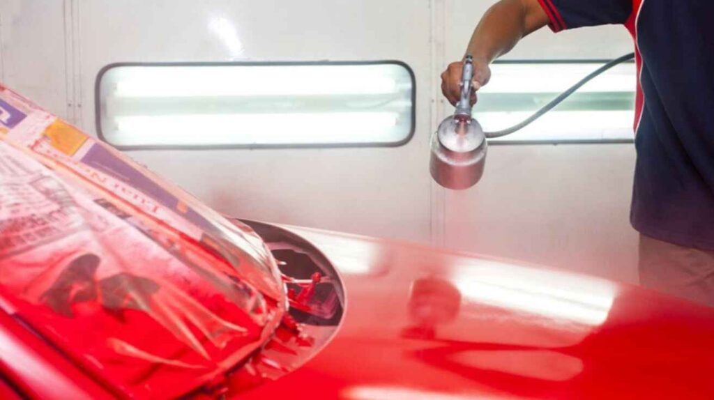 DIY car enthusiast applying spray-can primer on a car panel outdoors.