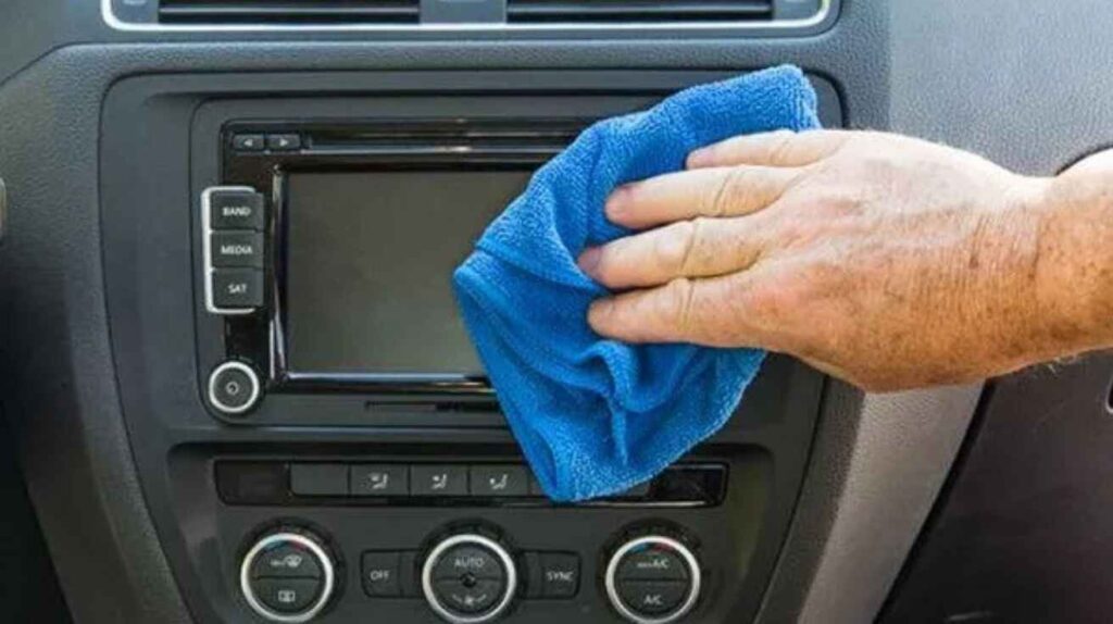 Cleaning car infotainment screen safely with microfiber cloth.